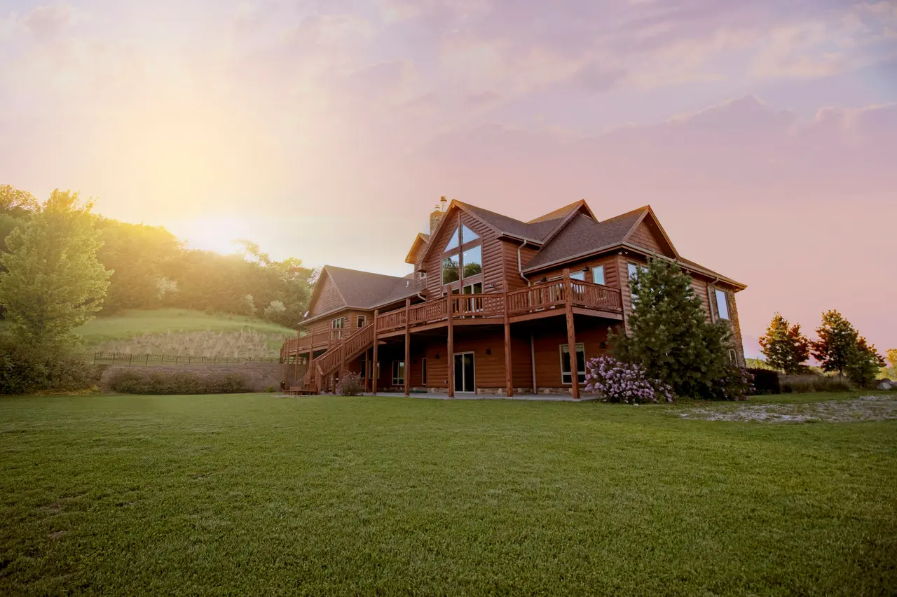 Casa de madeira com varanda em meio a um gramado, ao pôr do sol