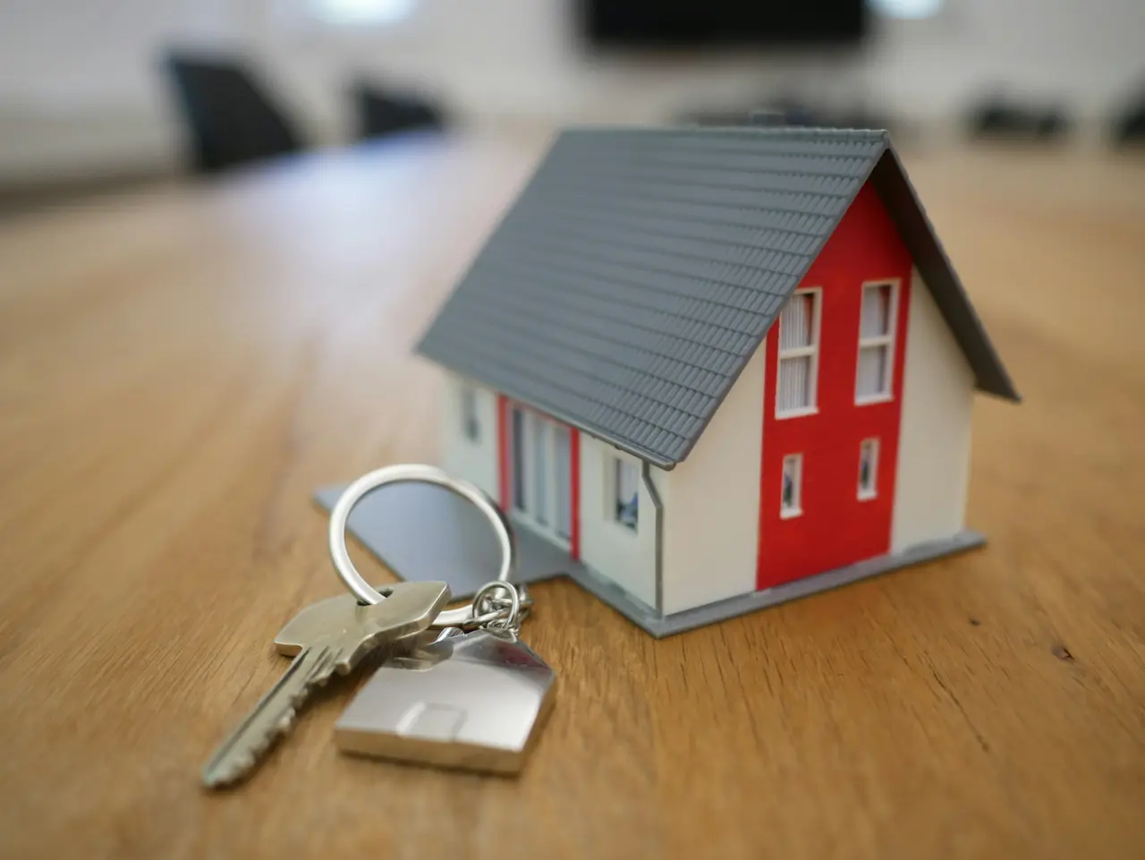 Miniatura de casa de telhado cinza ao lado de um molho de chaves sobre a mesa