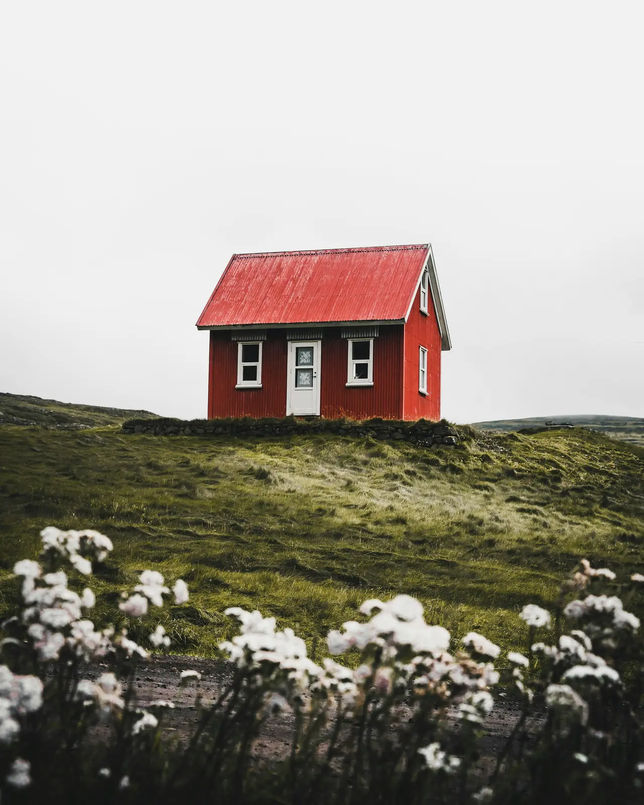 Casa pequena de telhado vermelho sobre um morro verde