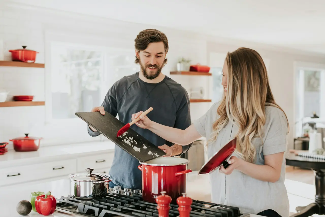 Casal sorrindo enquanto cozinha em uma cozinha clara e arejada
