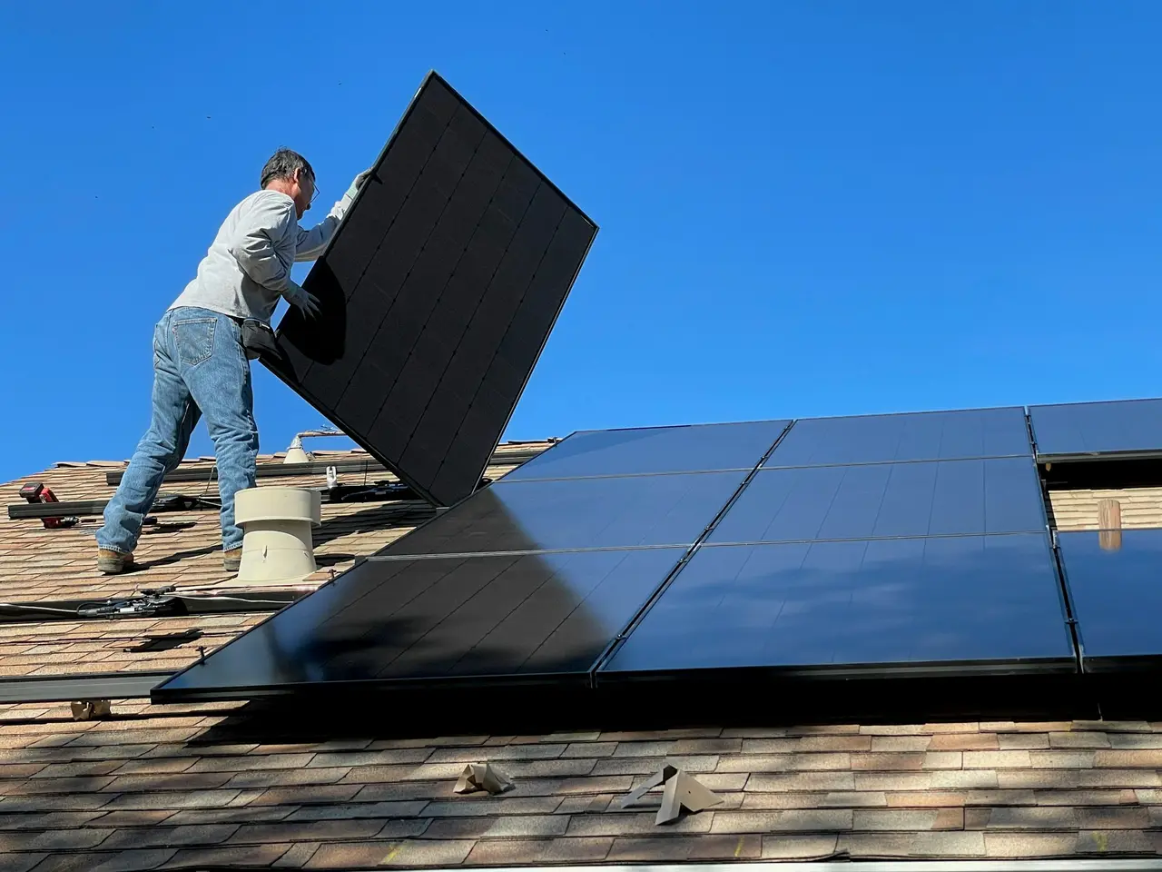 Instalador levantando um painel solar sobre um telhado de casa