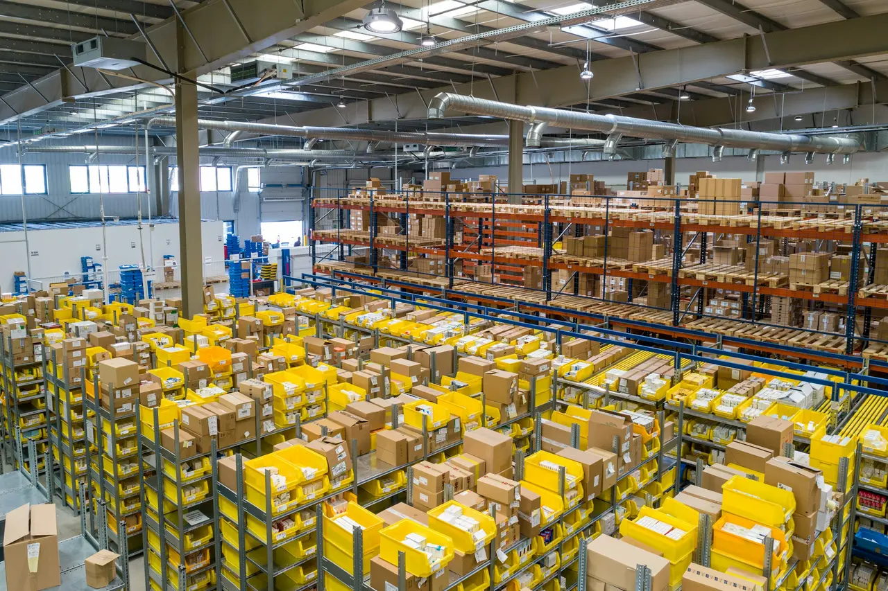 Interior de um galpão com prateleiras altas e paletes de mercadoria