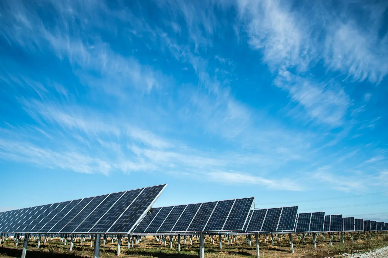 Longas fileiras de painéis solares sob um céu azul com nuvens finas