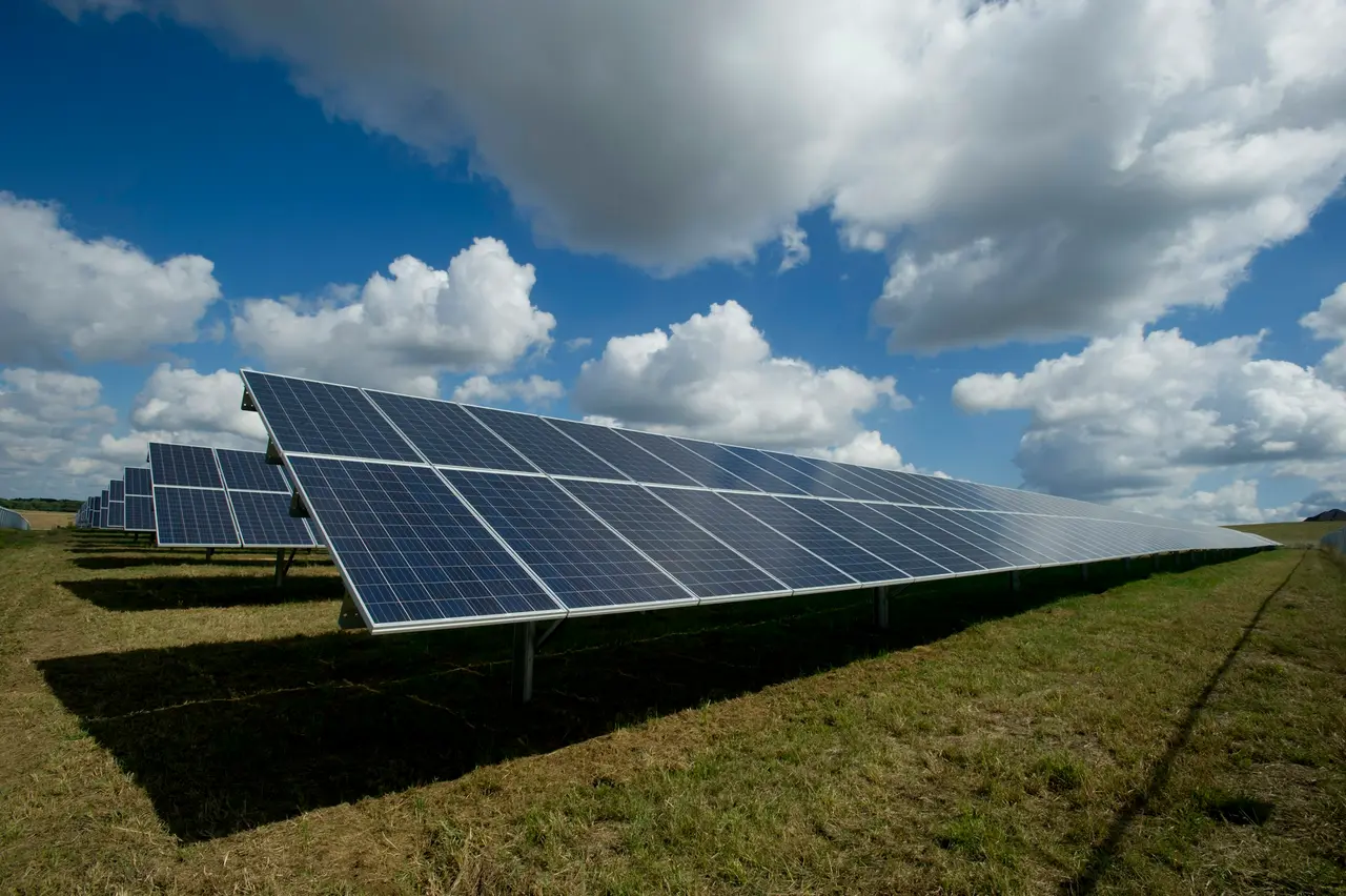 Usina solar com painéis em linha sob céu azul com nuvens
